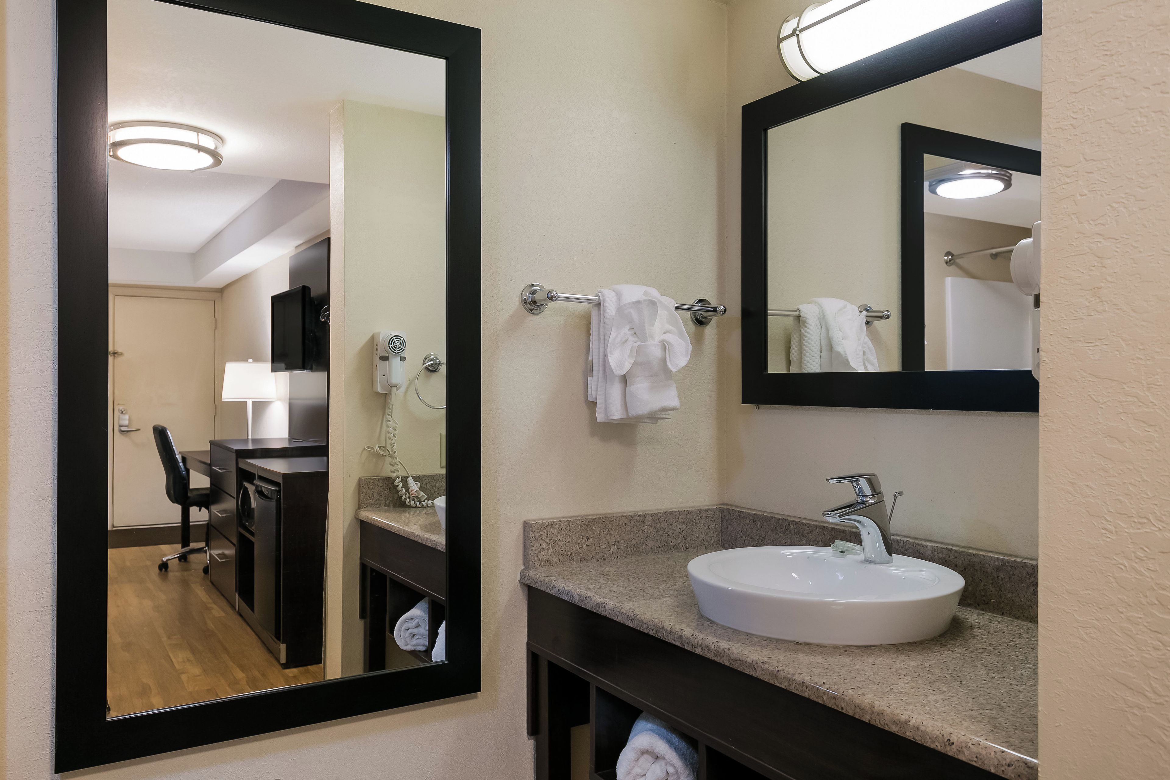 A bathroom with a large mirror, a sink, and a towel rack.