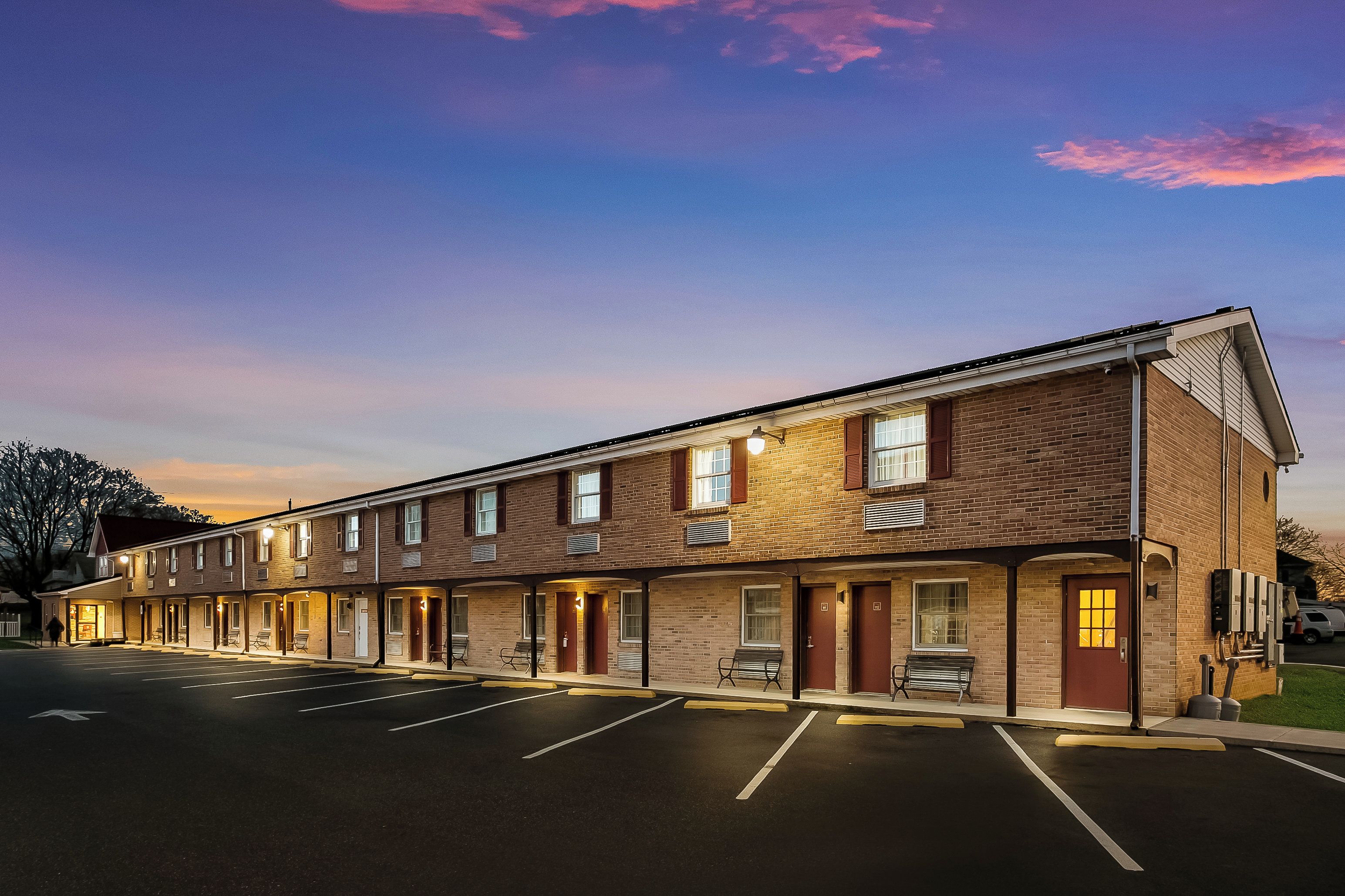 A multi-story brick building with a row of rooms, a parking lot, and a clear sky.