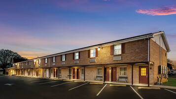 A multi-story brick building with a row of rooms, a parking lot, and a clear sky.