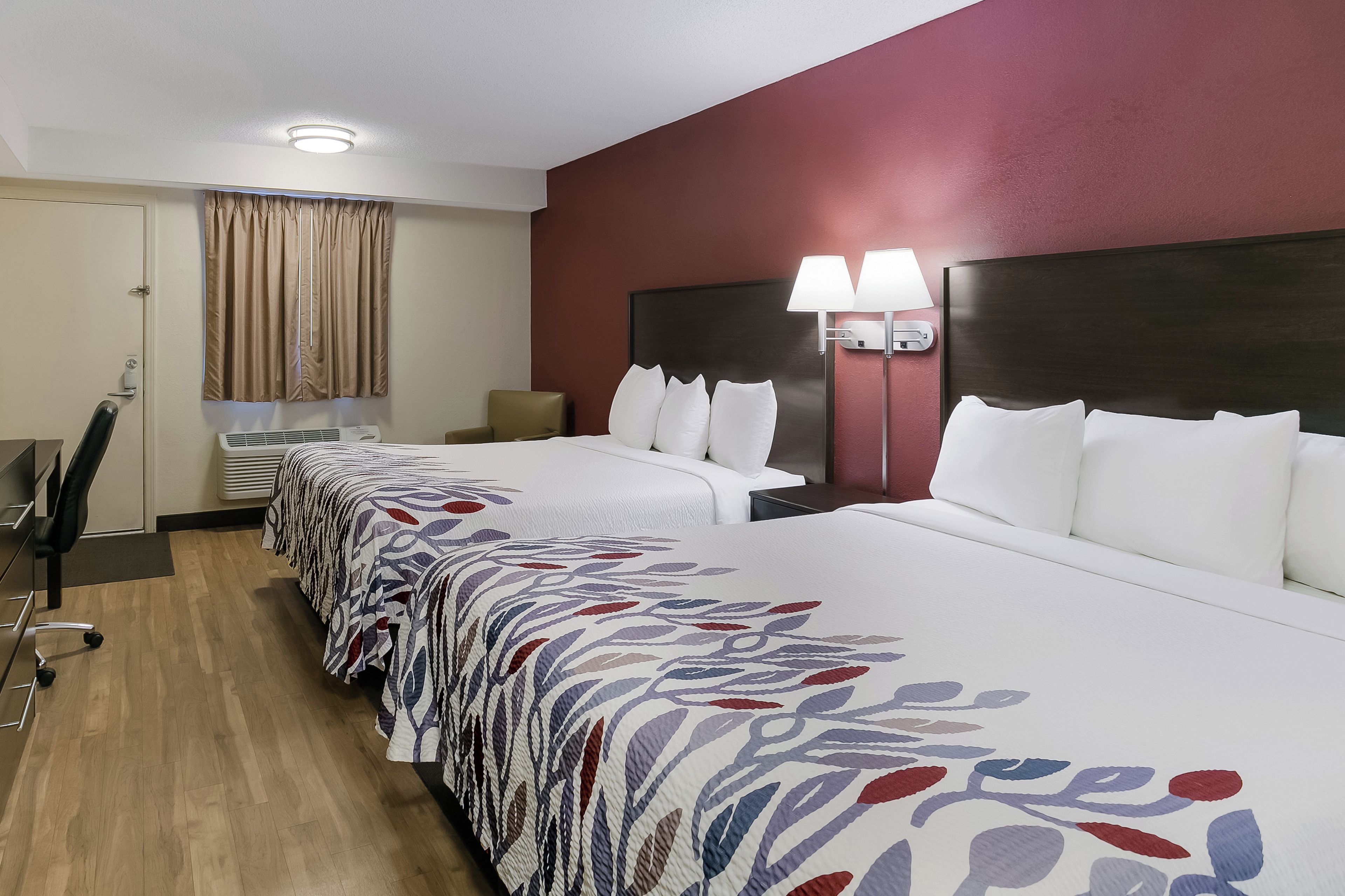 A hotel room with a large bed, a desk, a chair, and a lamp.