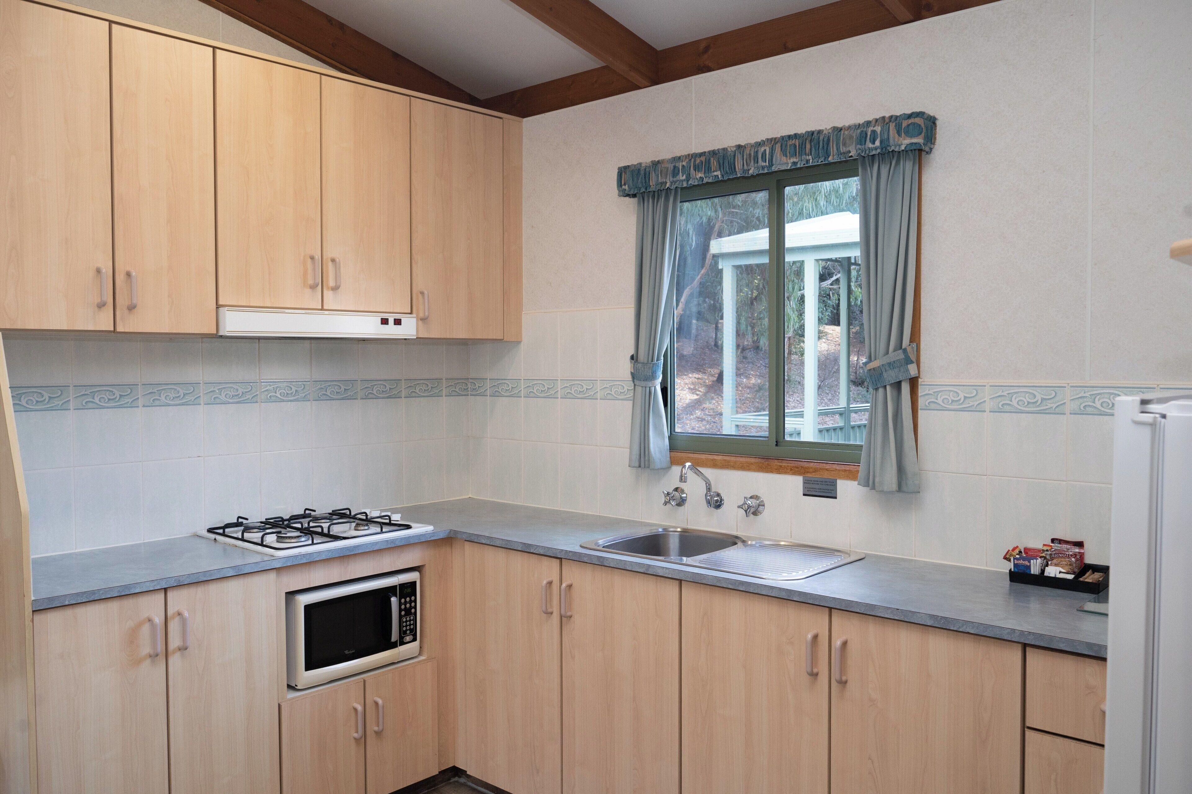 A kitchen with wooden cabinets, a gas stove, a microwave, a sink, and a window with curtains.