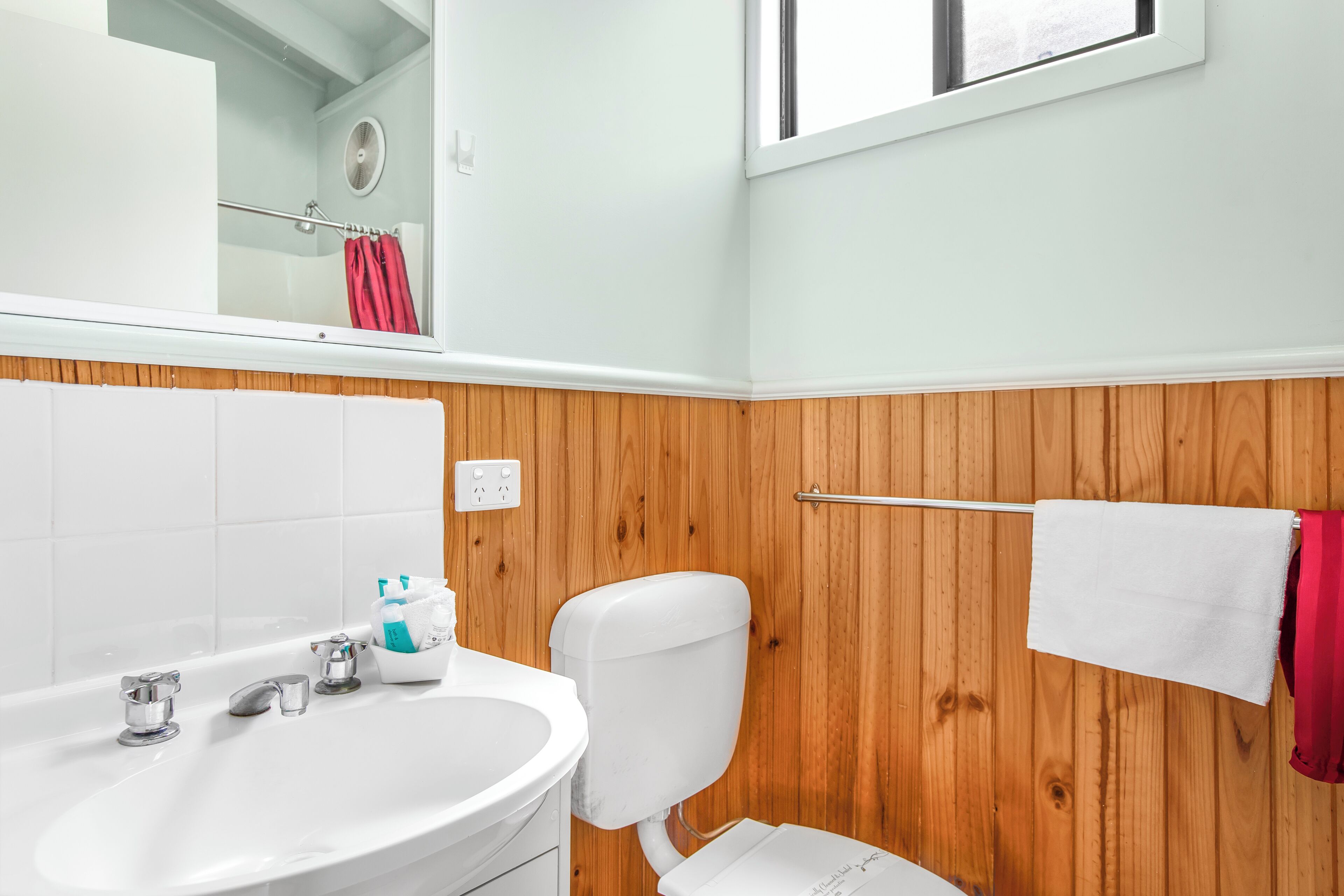 A bathroom with a white sink, wooden paneling, a toilet, and a red towel hanging on a rack.