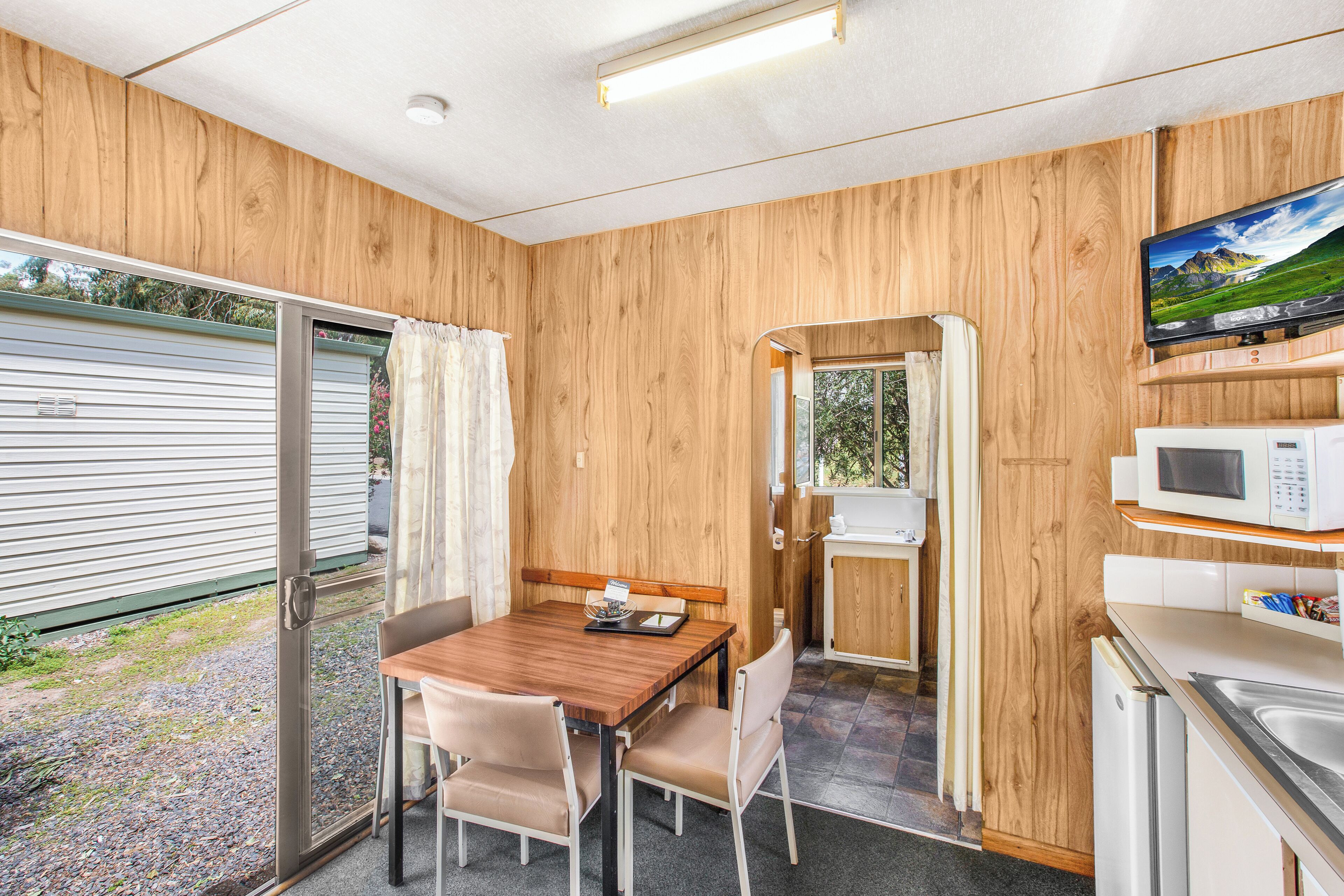 A compact kitchen with wooden walls, a dining area with a table and chairs, a microwave, and a television.