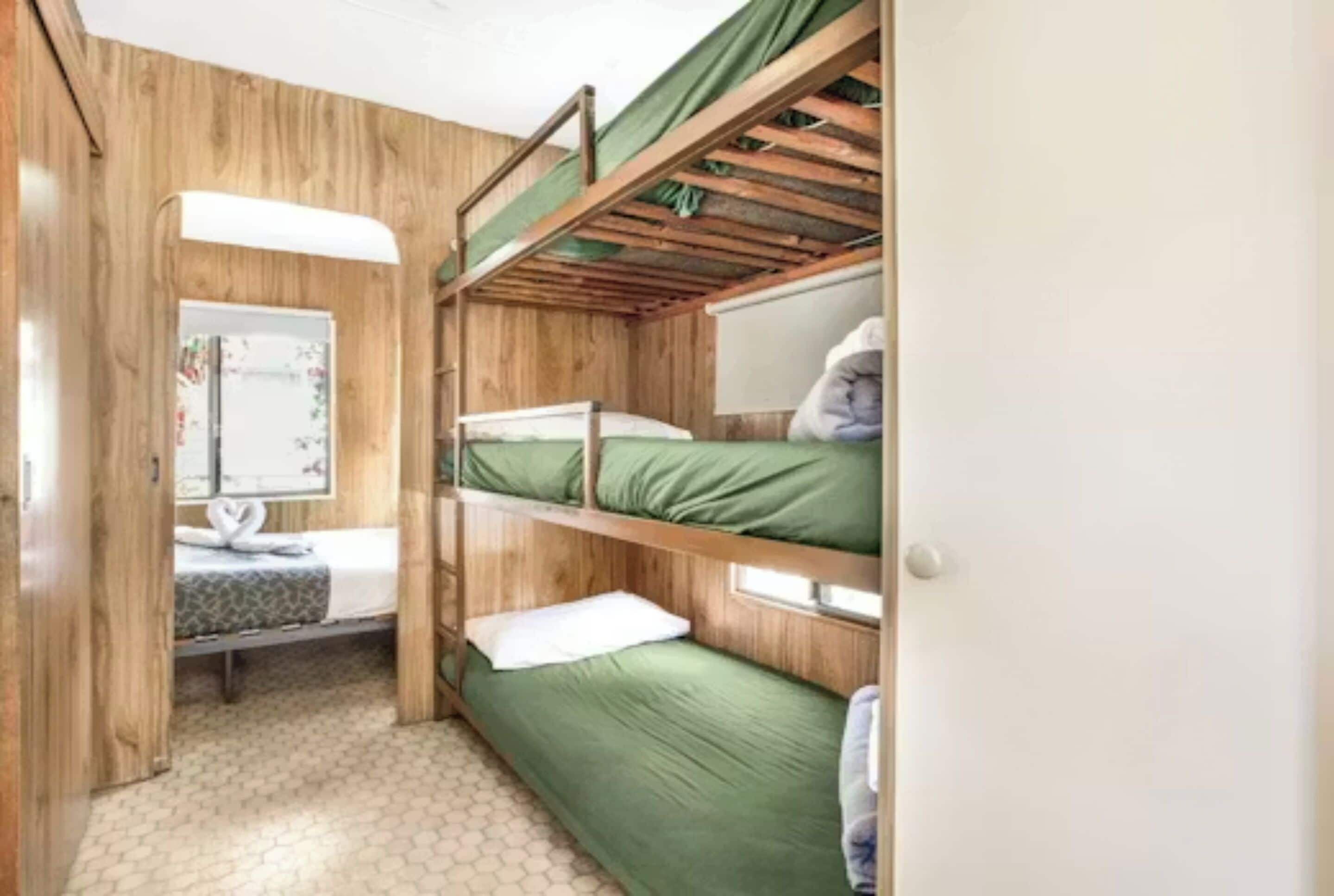 Une chambre avec un lit superposé, un plancher en bois, un petit bureau avec un miroir et une fenêtre.