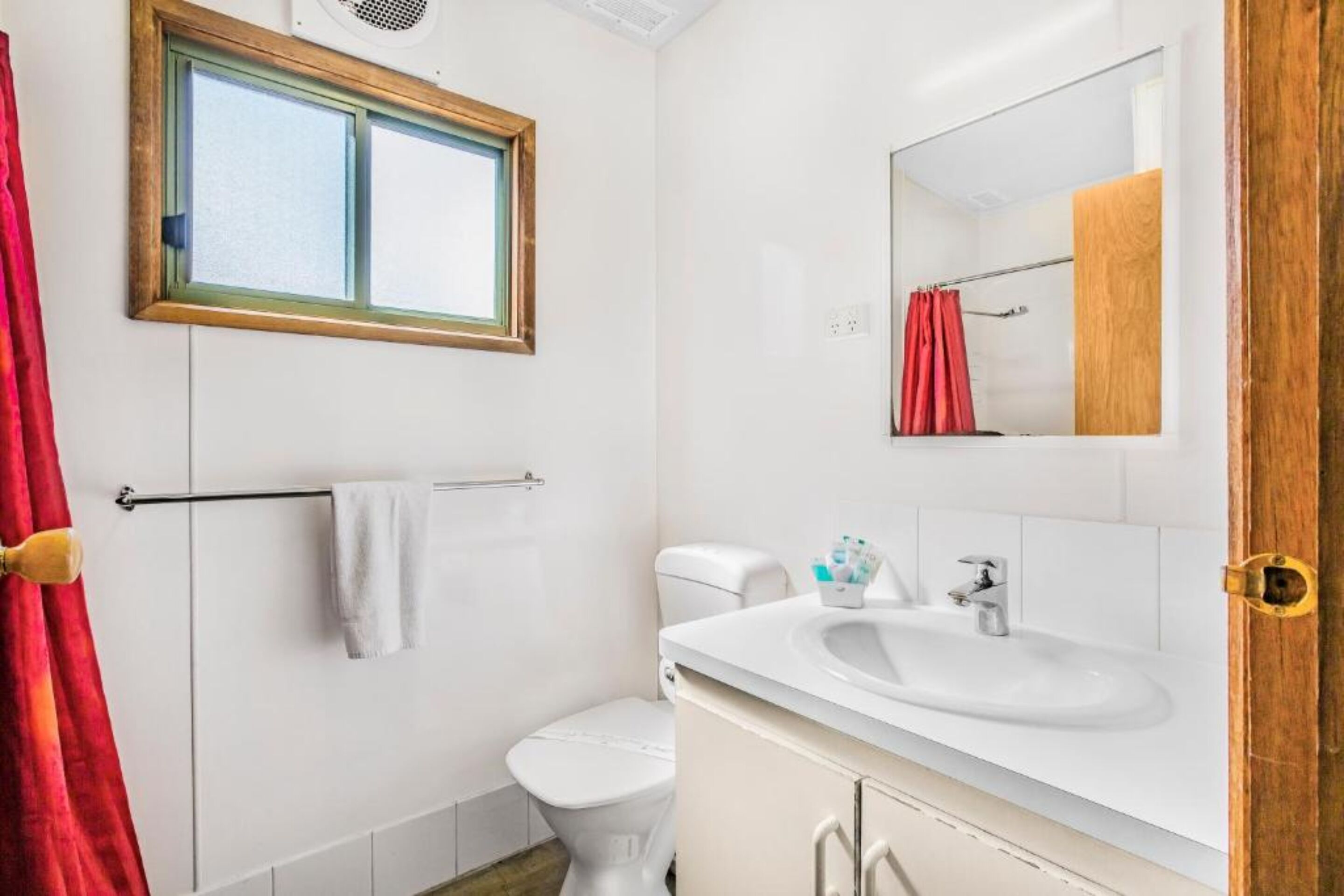 A bathroom with a white sink, a toilet, a window, and a shower curtain.