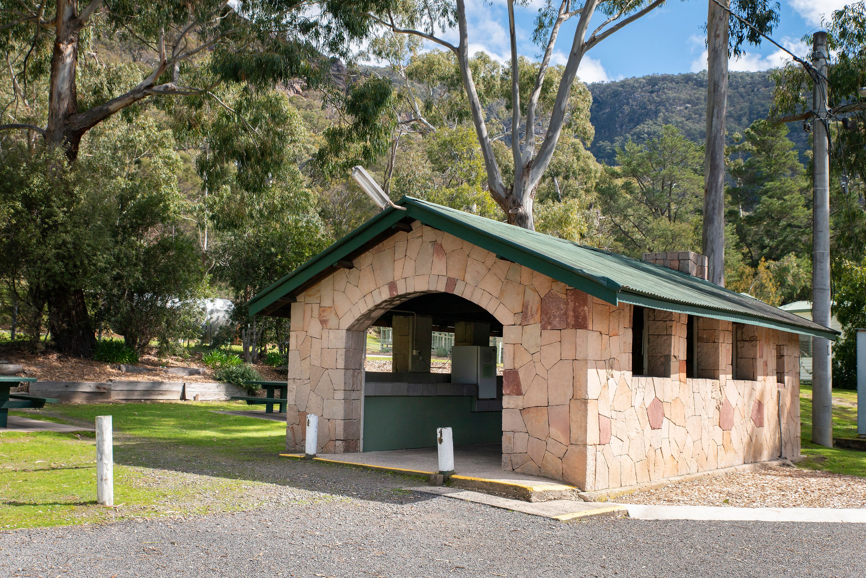 A stone structure with a green roof, likely a restroom or small shelter, surrounded by trees and a grassy area.