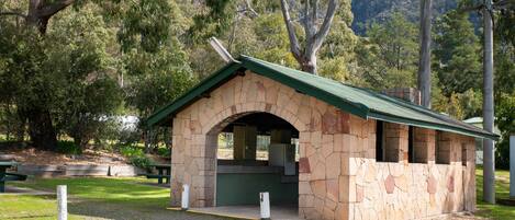 A stone structure with a green roof, likely a restroom or small shelter, surrounded by trees and a grassy area.