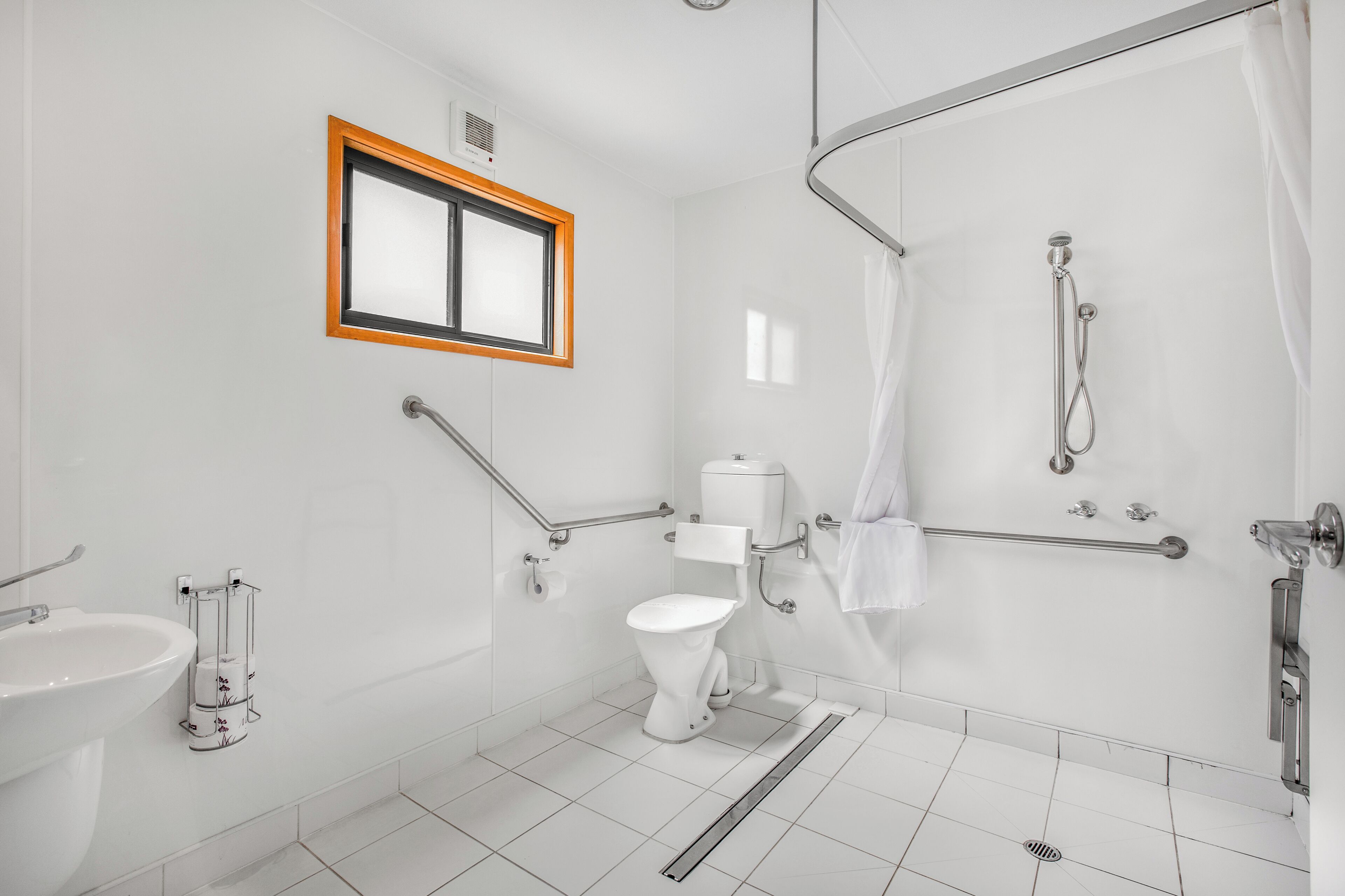 A modern bathroom with a toilet, bidet, and shower. There is a window with a wooden frame and a towel rack.