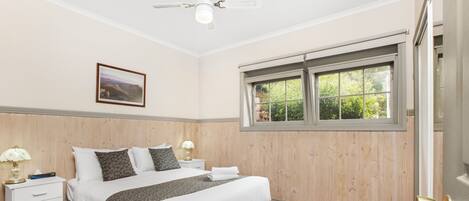 A neatly arranged bedroom with a bed, bedside tables, a window, and a ceiling fan.