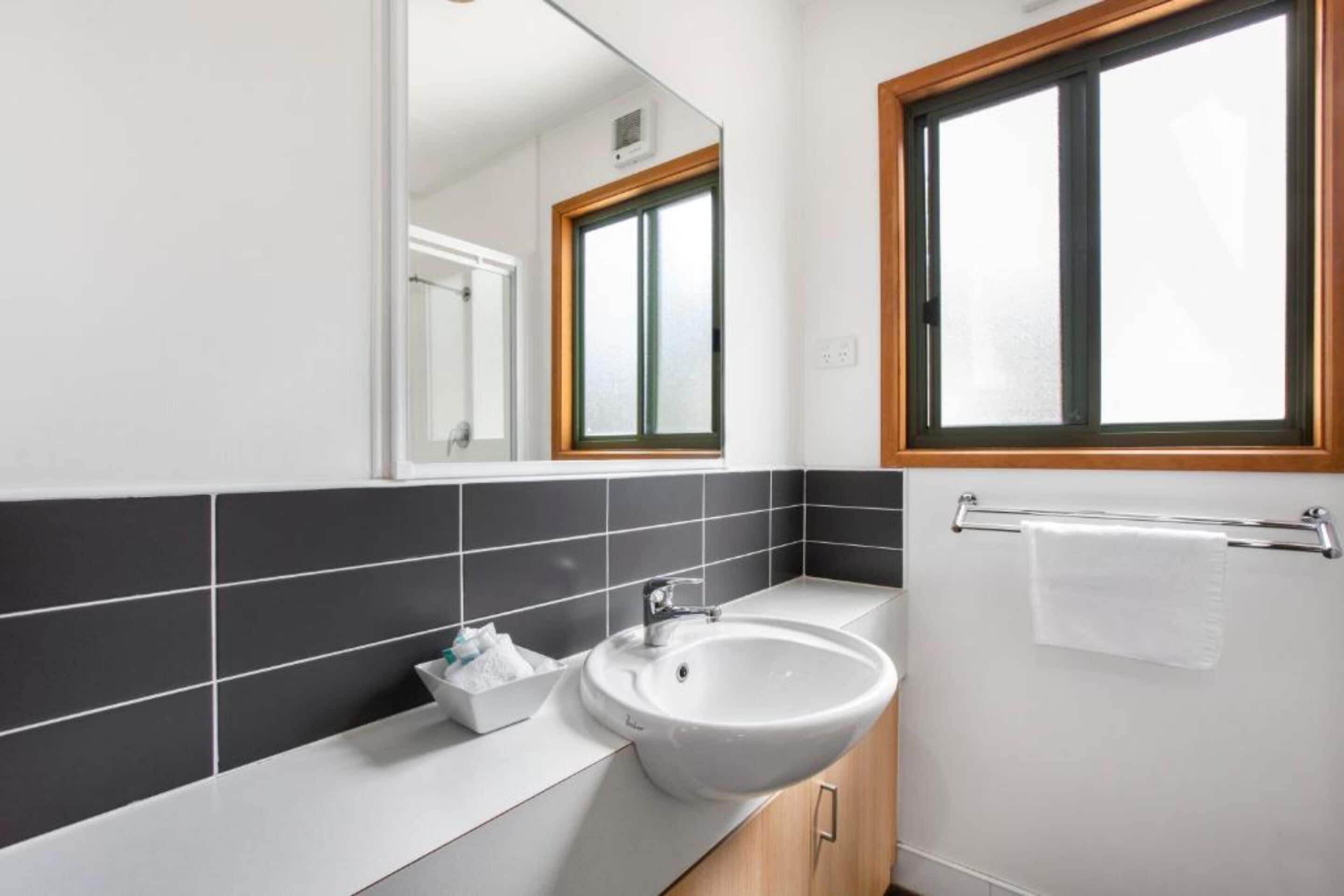Un bagno moderno con lavandino bianco, piastrelle bianche e nere, un davanzale di legno e un porta asciugamani.