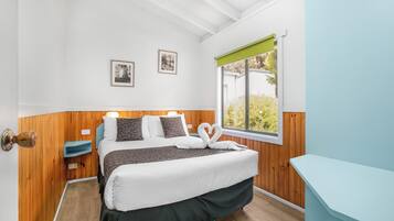 A neatly arranged bedroom with a bed, bedside tables, framed pictures on the wall, and a window with a view of greenery.