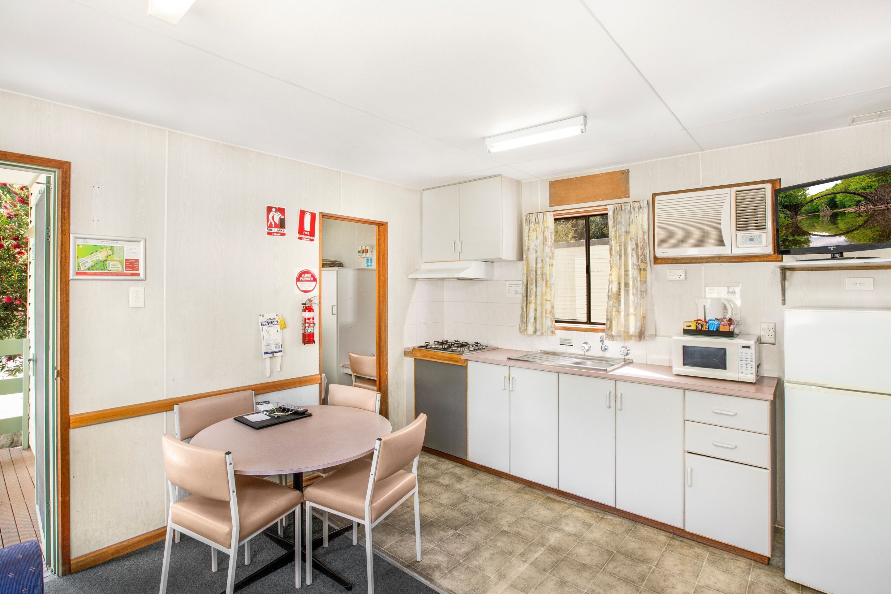 A compact kitchen with white cabinets, a microwave, and a gas stove. There is a dining table with chairs and a small window with curtains.