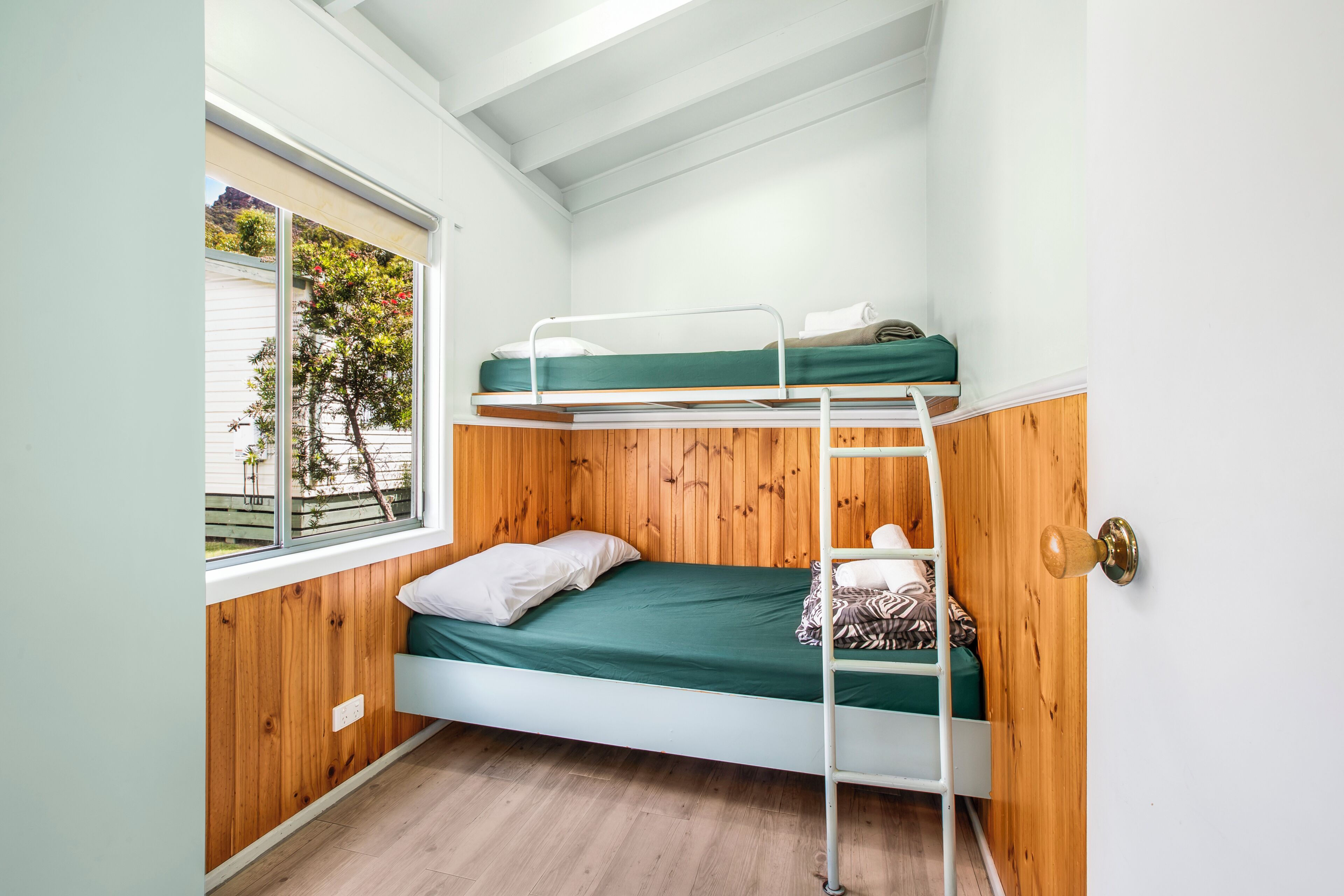 Een slaapkamer met een stapelbed, raam, houten lambrisering en een deur.