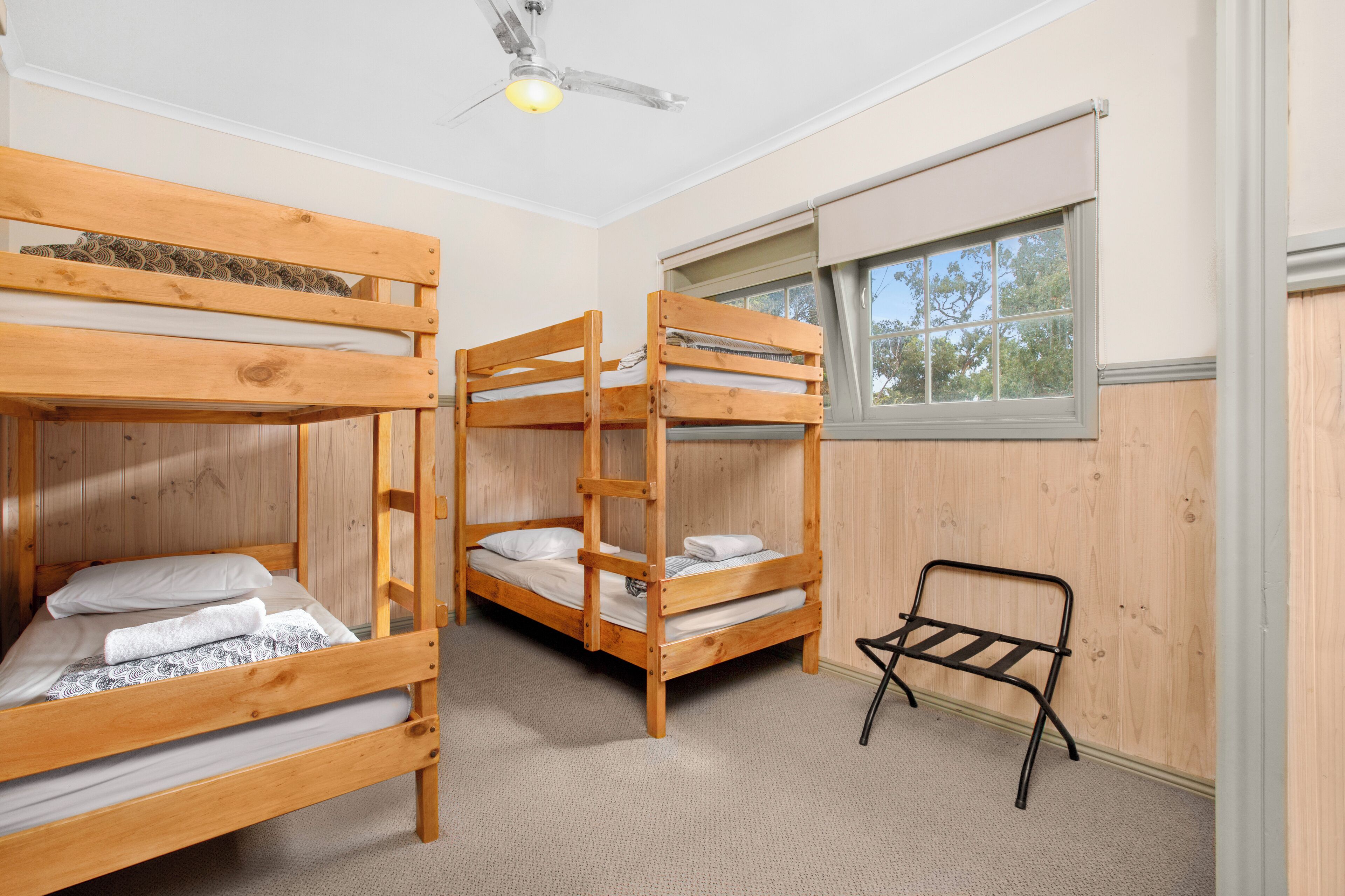 A room with three bunk beds, a ceiling fan, and a window with a view of trees.