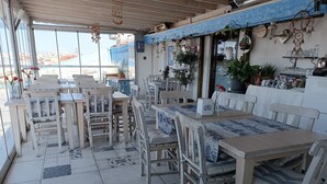 A restaurant with outdoor seating, wooden tables and chairs, potted plants, and a view of the cityscape. - The City Residence (Çanakkale)