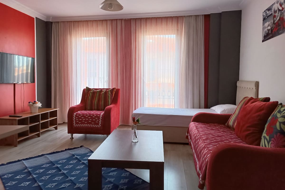 Ein Zimmer mit einem Bett, einem roten Sessel, einer Couch, einem Fernseher und einem Tisch.