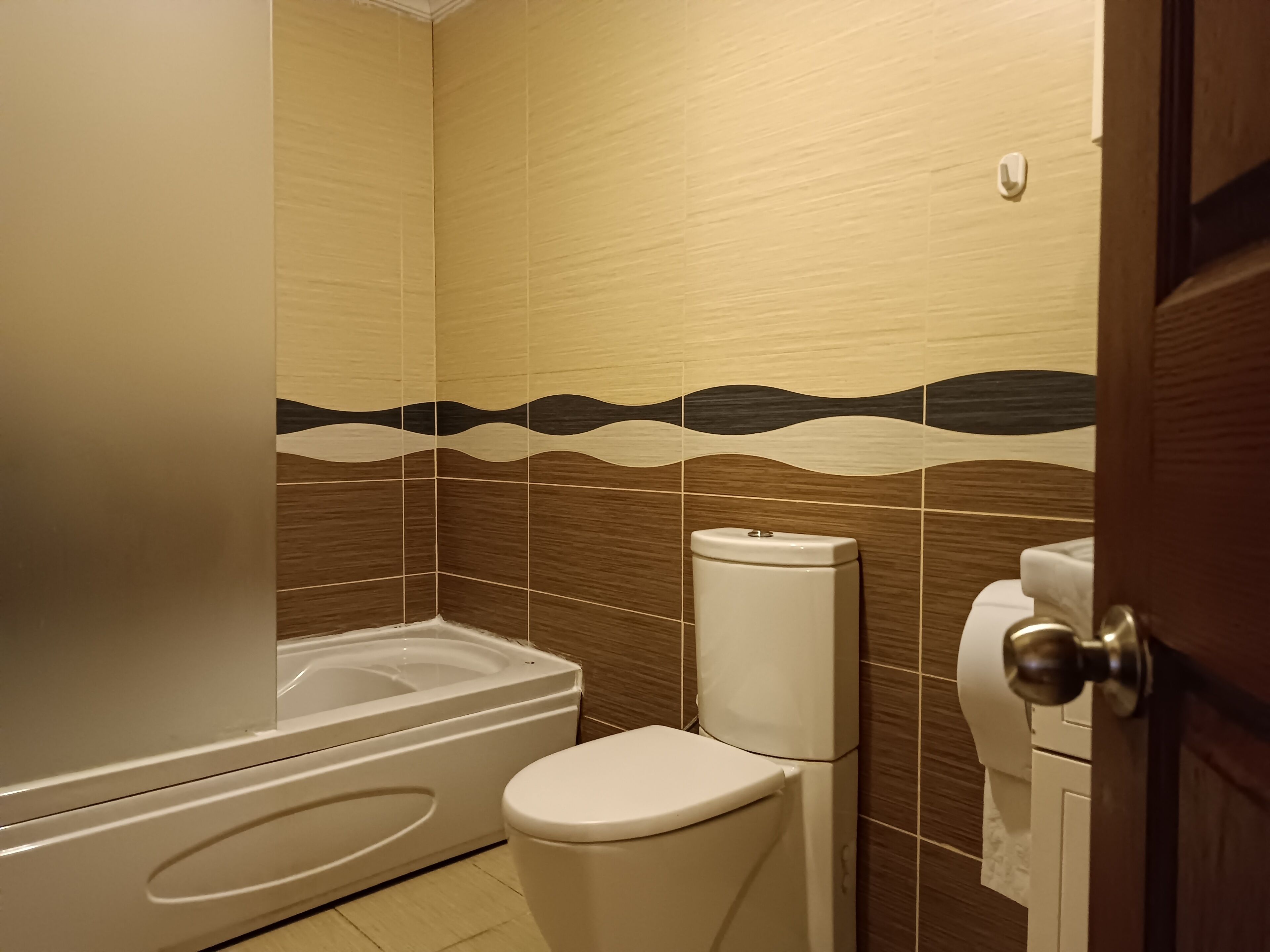 A bathroom with a bathtub, toilet, and a towel dispenser.