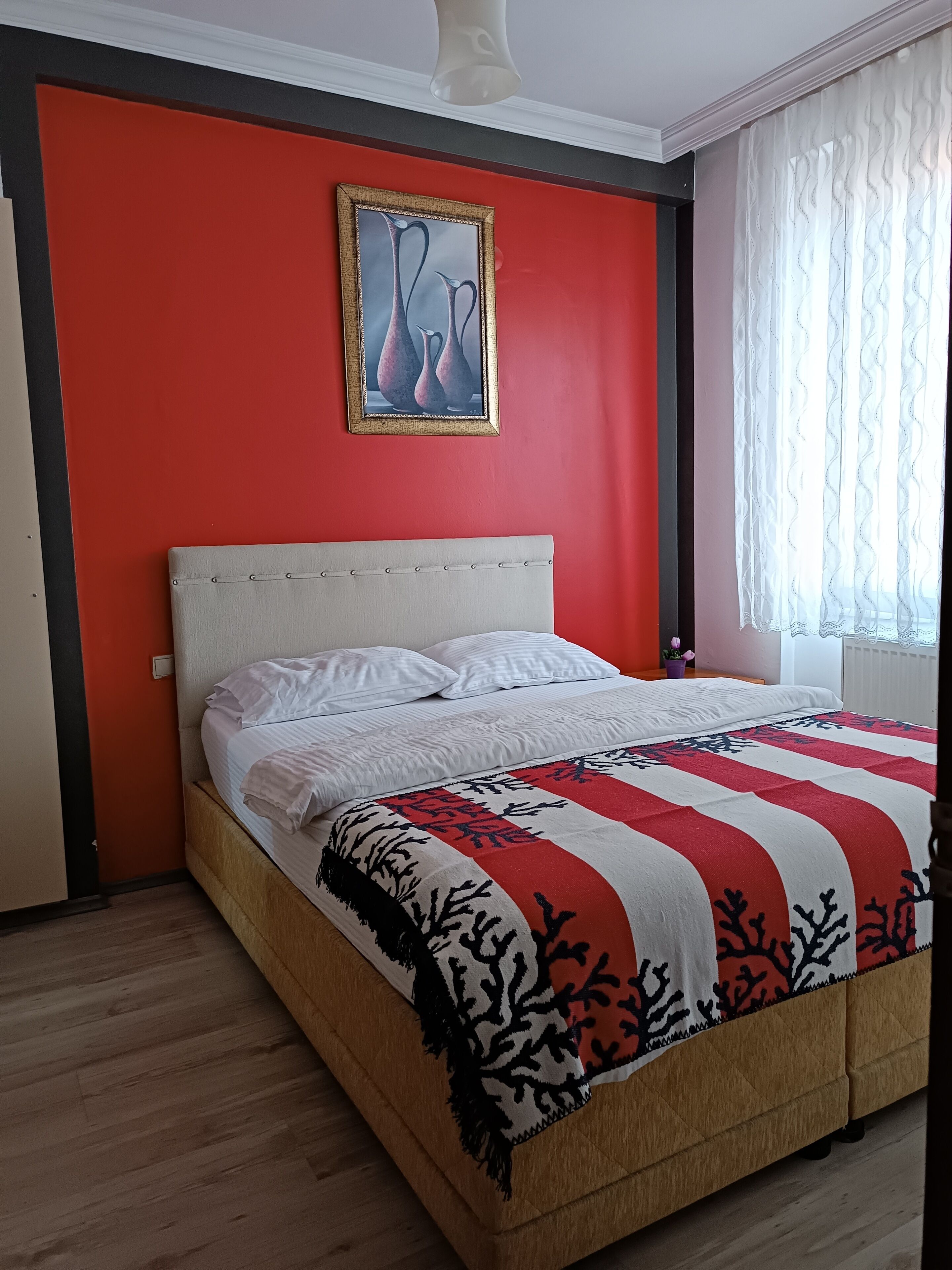 A bed with a white headboard, a red and white striped blanket, and a framed picture on the wall.