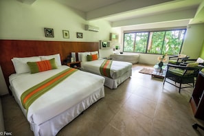 A hotel room with two beds, a desk, a chair, and a large window with a view of greenery. - Terrazas de Golf Boutique Hotel (La Asunción)