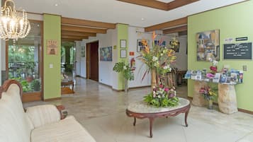A lobby with a reception desk, a chandelier, a sofa, and a decorative plant centerpiece.