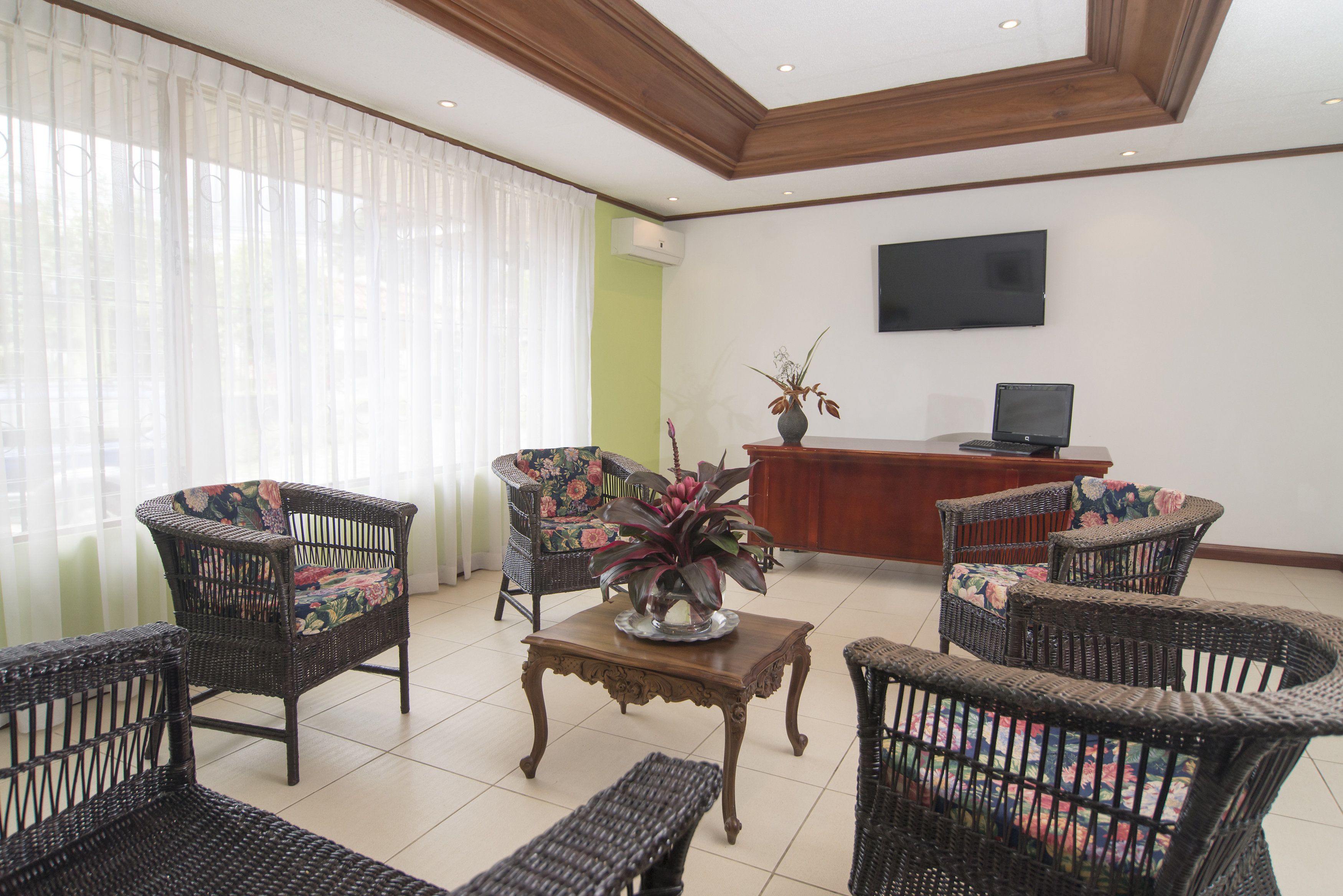 Un hall de hotel con mobiliario de mimbre, una recepción de madera y un televisor de pantalla plana.