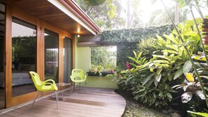 Eine Holzterrasse mit zwei Stühlen, einem überdachten Patio und üppigem Grün drumherum.