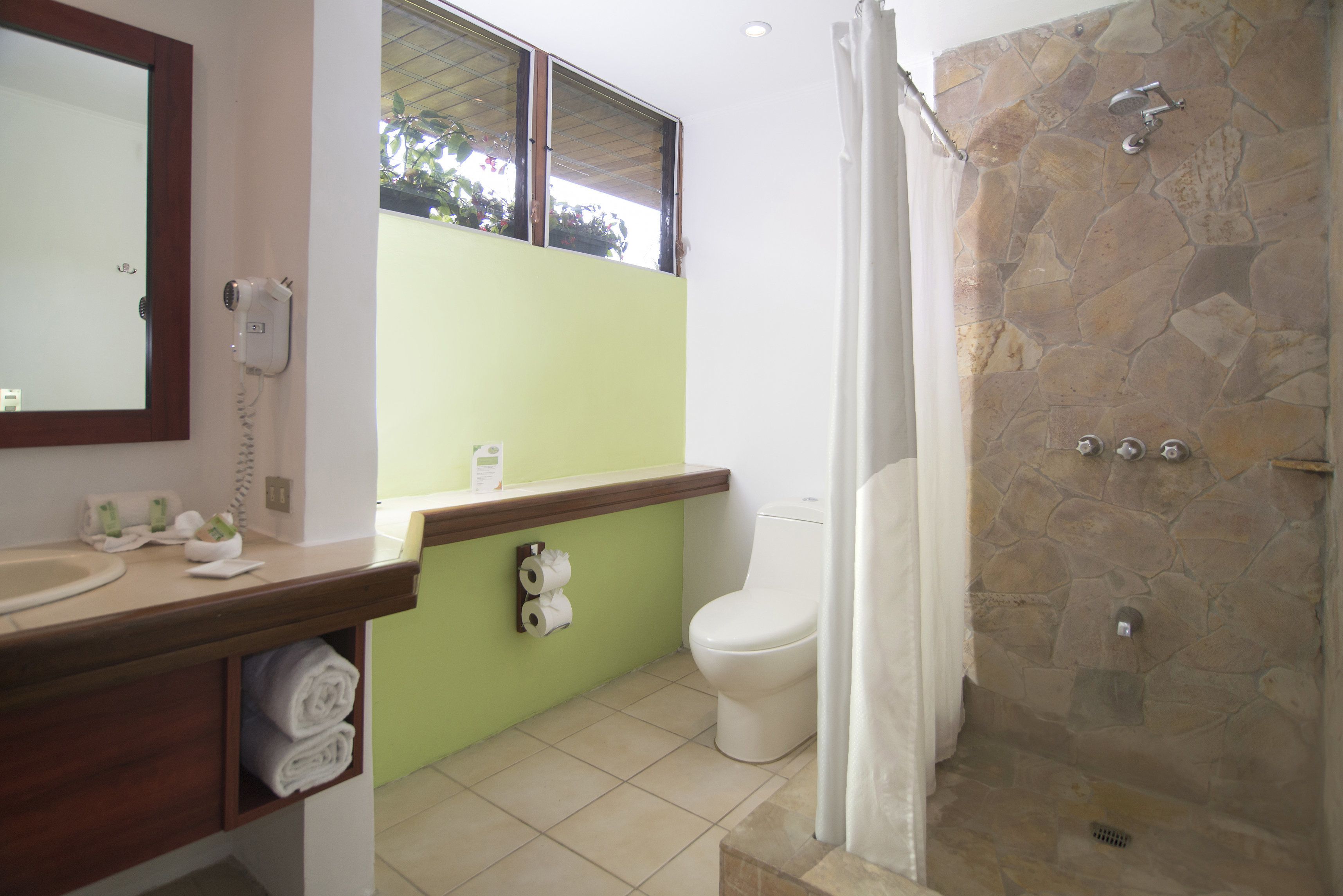 Un baño con pared de ducha de piedra, inodoro y lavabo con espejo.