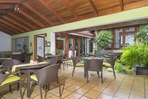 Une terrasse extérieure avec des meubles en osier, un sol carrelé et des plantes en pot.