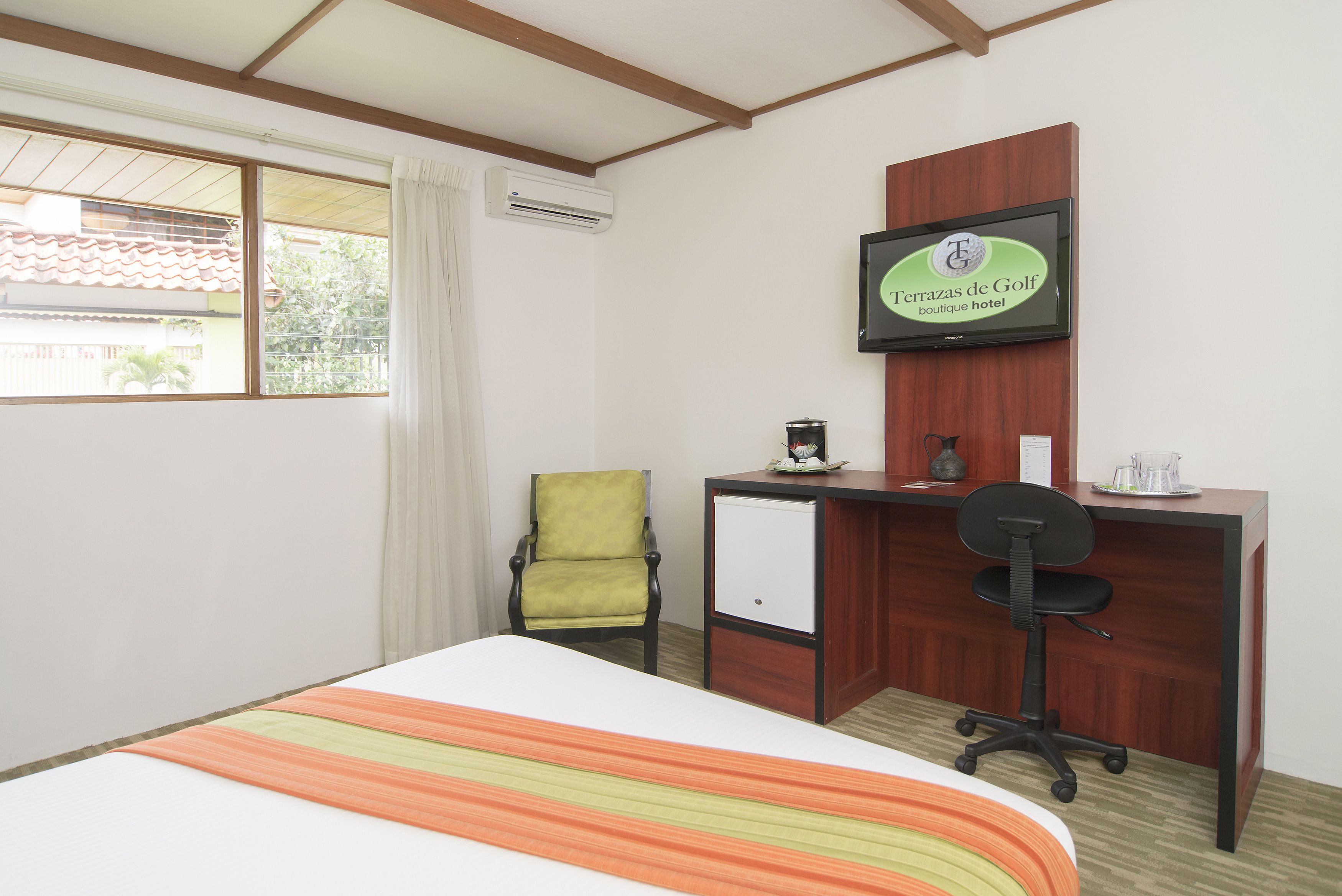 A hotel room with a bed, a desk, a chair, and a television on the wall.