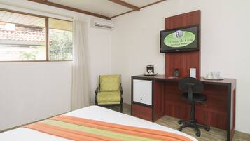 A hotel room with a bed, a desk, a chair, and a television on the wall.