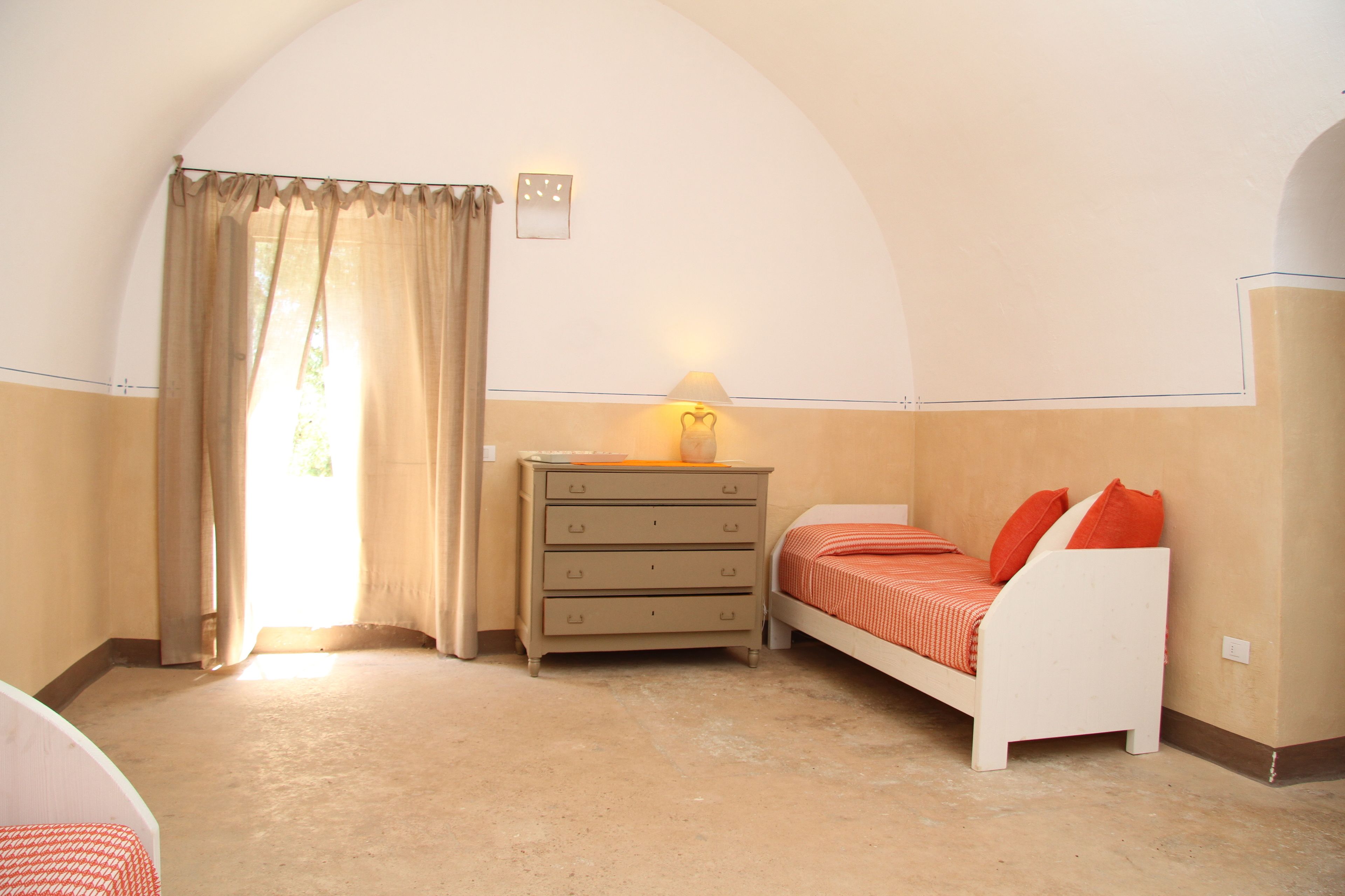 A bedroom with a bed, a dresser, a lamp, and a window with curtains.