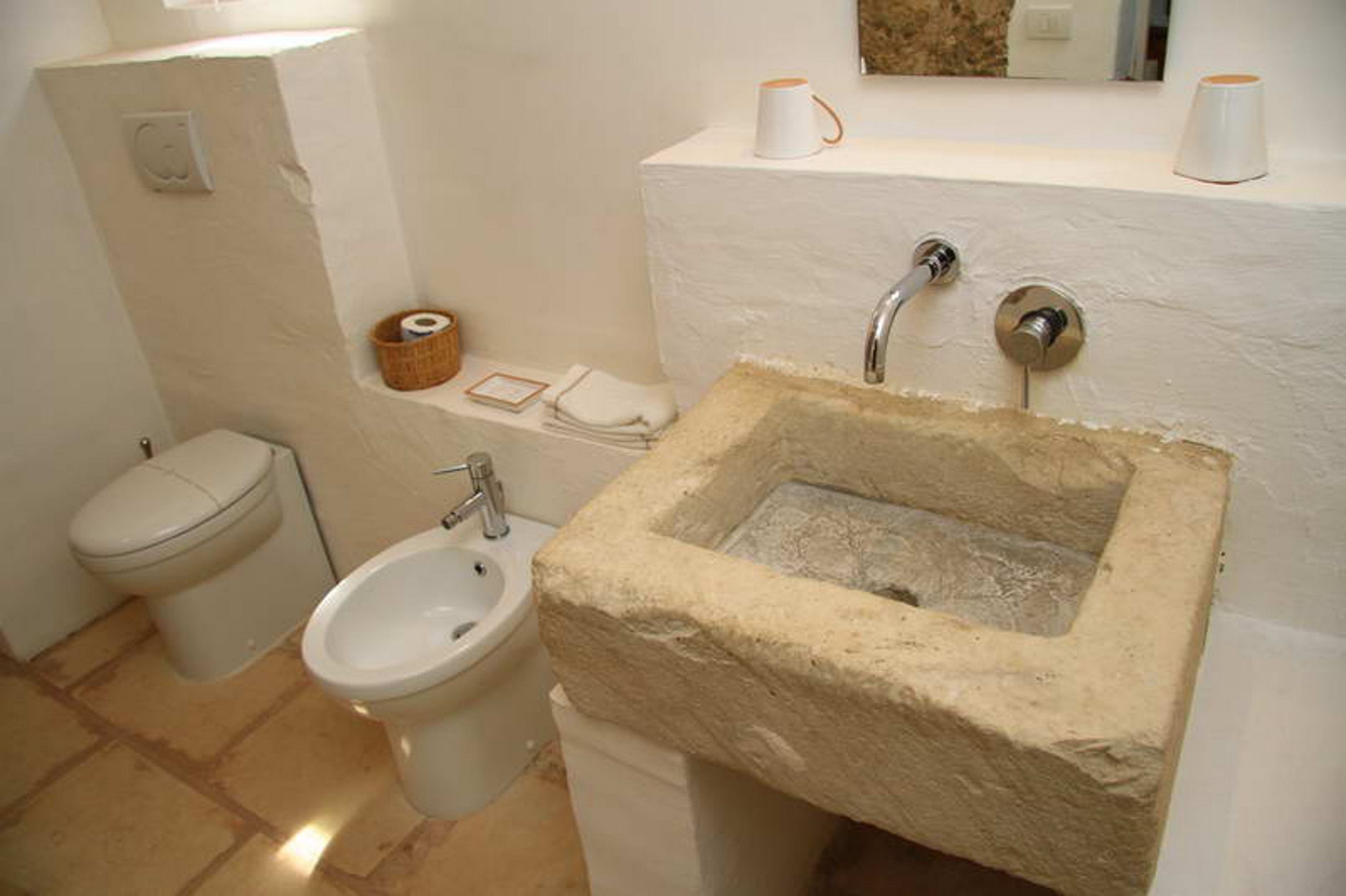 A bathroom with a stone sink, a toilet, and a bidet.
