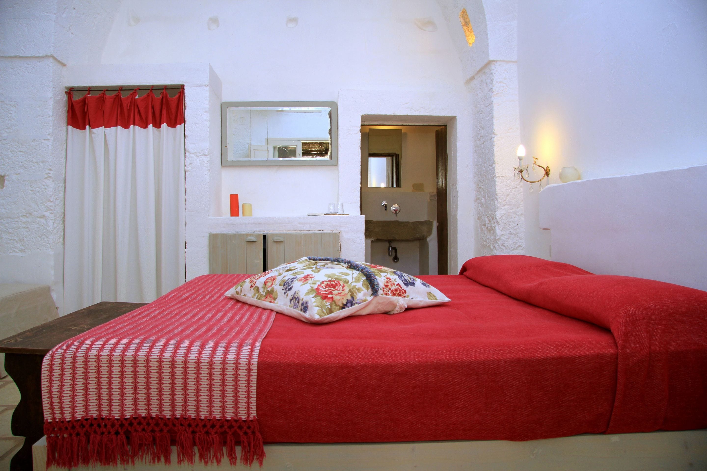 Une chambre avec une couvre-lit rouge, un coussin à motifs floraux et un plaid rouge et blanc.