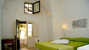 Ein Zimmer mit einem Bett, einem Sessel, einem Tisch und einer Tür zu einem Außenbereich.
