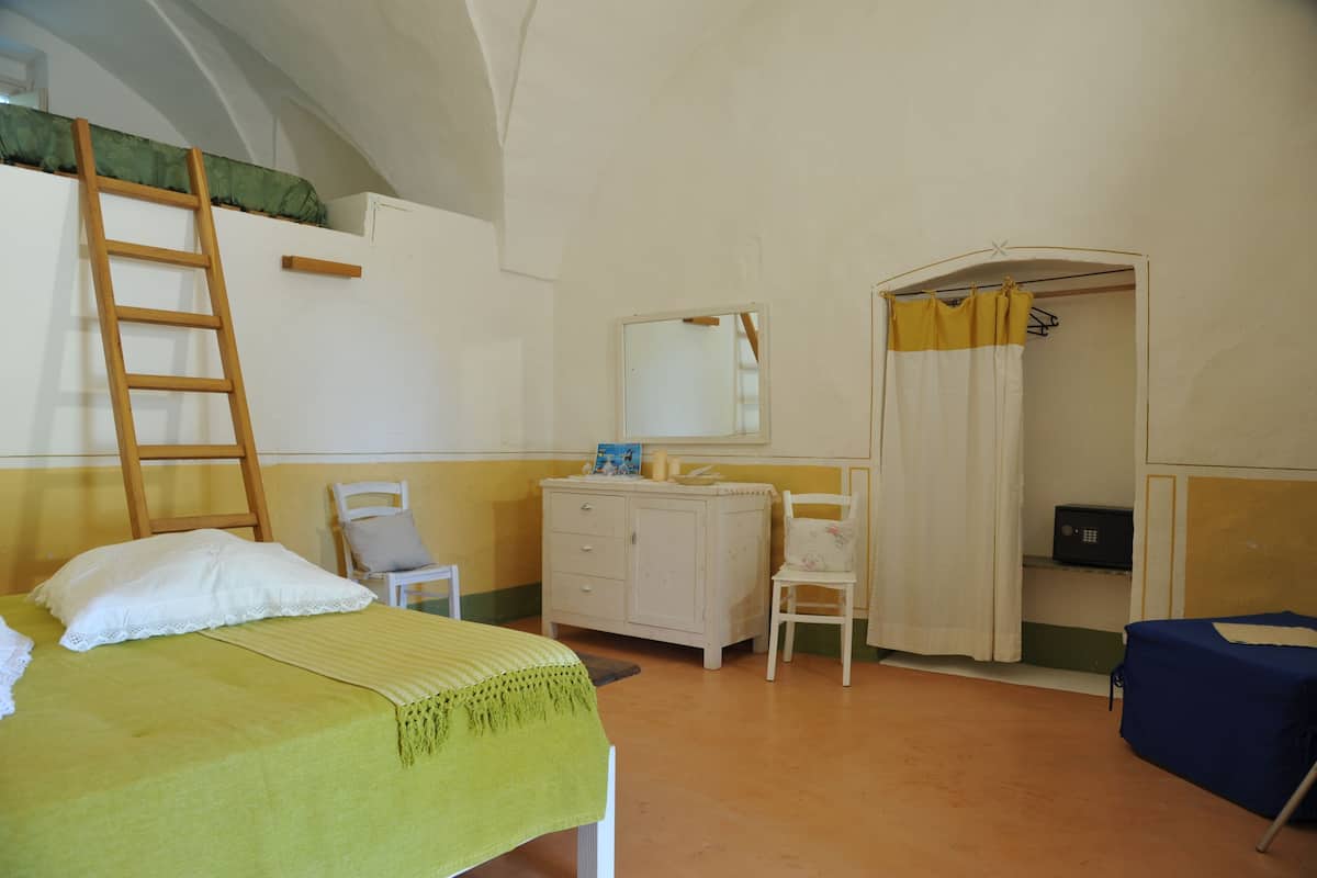 A room with a bunk bed, a desk with a mirror, a chair, a wardrobe, and a bathroom with a shower curtain.