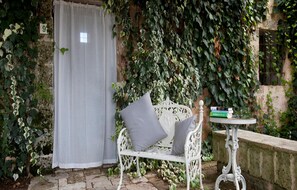 A white wrought-iron bench with grey cushions, a white table with a book, and a white door with a number 9 sign. - Masseria Cristo (Ugento)