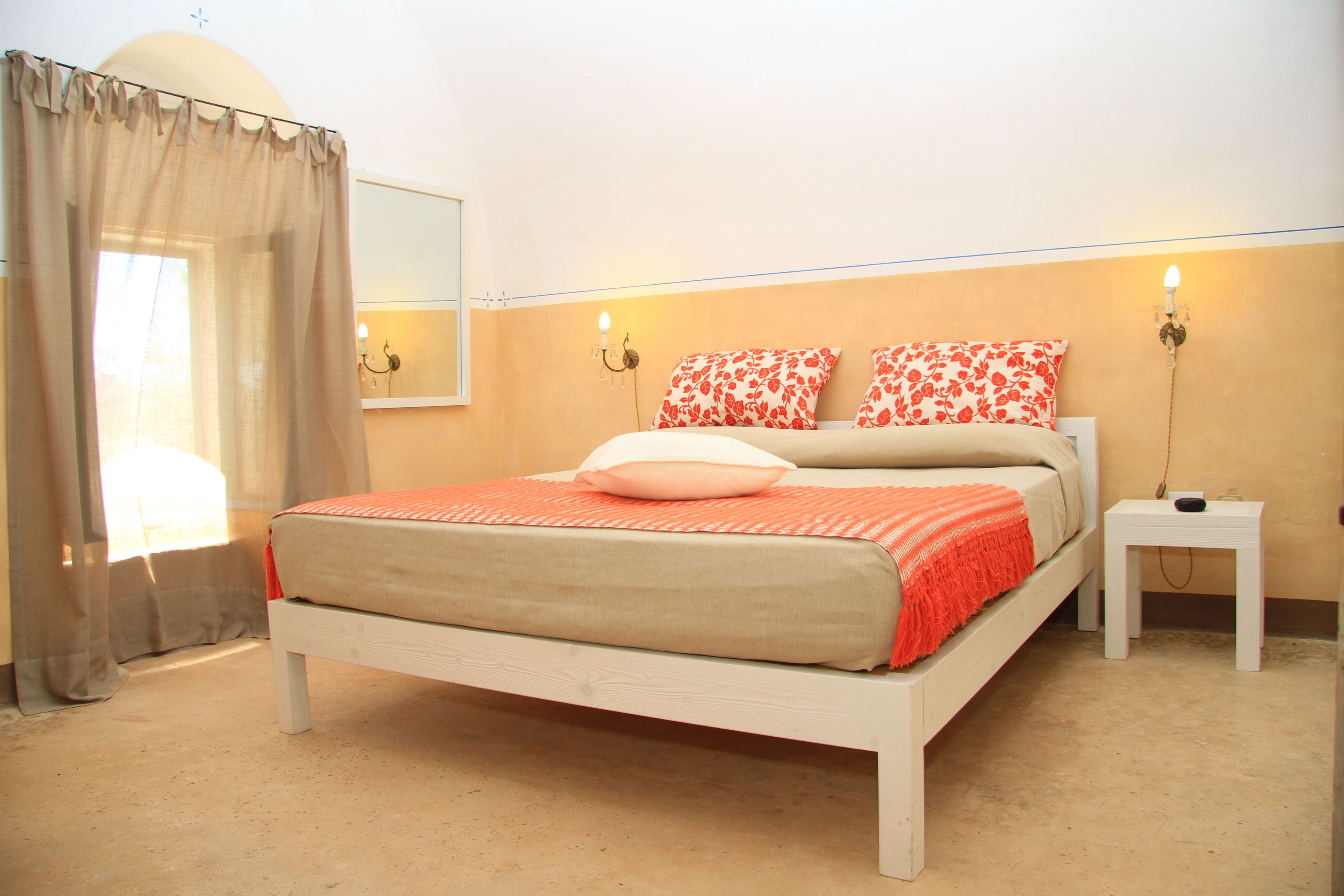 Ein Schlafzimmer mit einem Bett, einem Nachttisch, einem Spiegel und einer Wandleuchte.