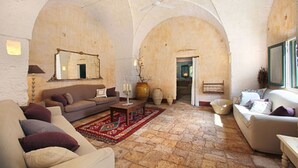 Ein großzügiges Wohnzimmer mit hohen Decken und Rundbogenwänden, ausgestattet mit Sofas und einem Couchtisch, sowie einem großen Spiegel an der Wand.