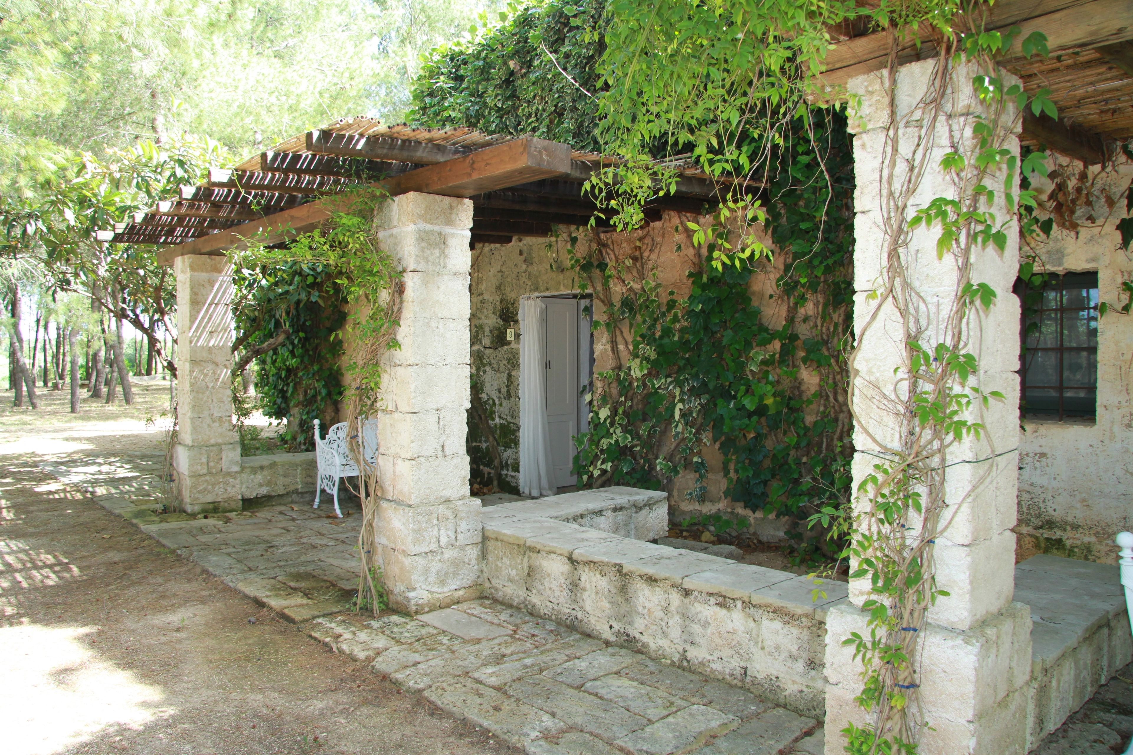 Ein rustikales Gebäude mit einer Stein-Fassade, einer Holz-Pergola und Stufen, die zu einer Tür führen.