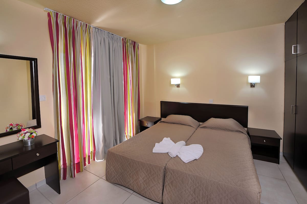 Une chambre d’hôtel avec un lit, des tables de chevet, une commode, un miroir et une fenêtre avec des rideaux.