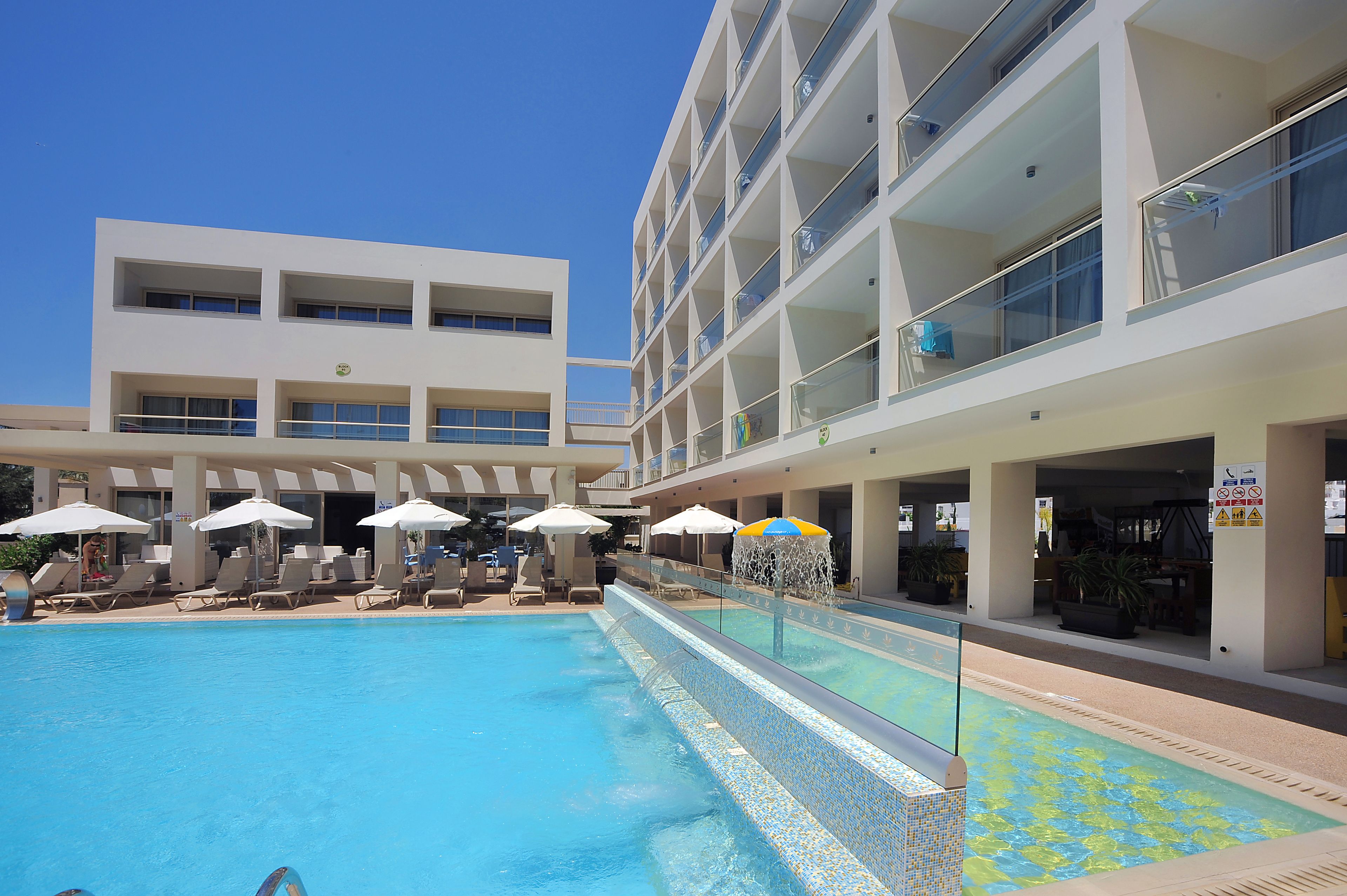 A modern hotel with a swimming pool, sun loungers, and umbrellas.