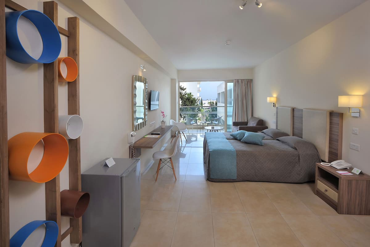 Une chambre d’hôtel moderne équipée d’un lit, d’un bureau et de chaises, d’un balcon avec vue et d’un téléviseur fixé au mur.