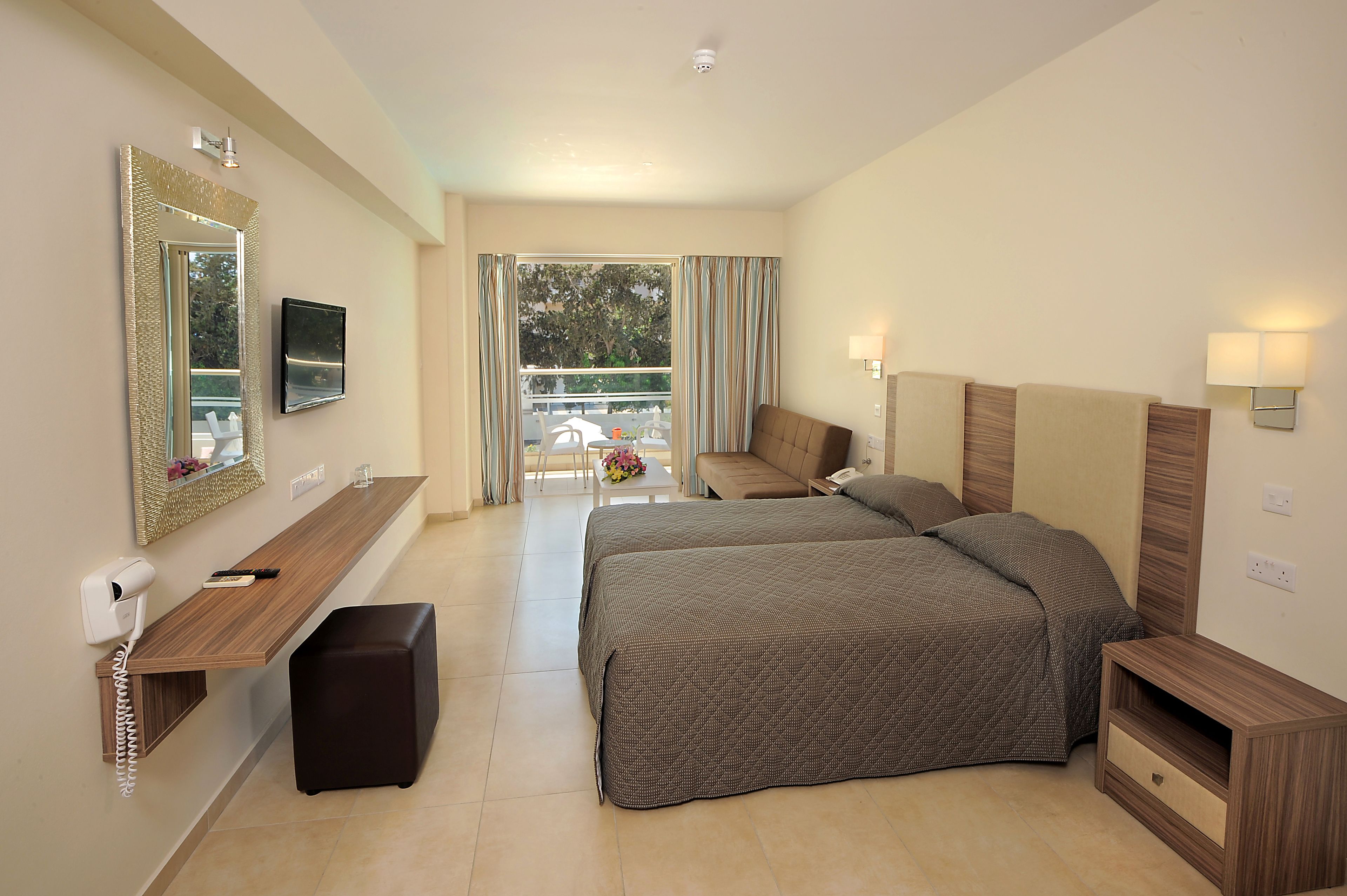 Une chambre d’hôtel avec un grand lit, une table de chevet, un miroir, une télévision et une vue sur le balcon extérieur.