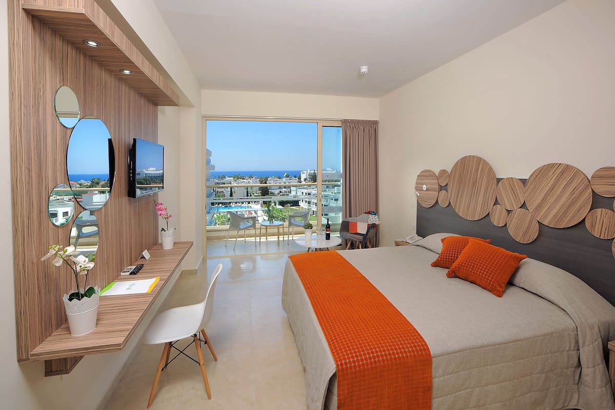 Une chambre d’hôtel moderne dotée d’un grand lit, d’un bureau avec un ordinateur, d’une télévision et d’un balcon offrant une vue sur la ville.