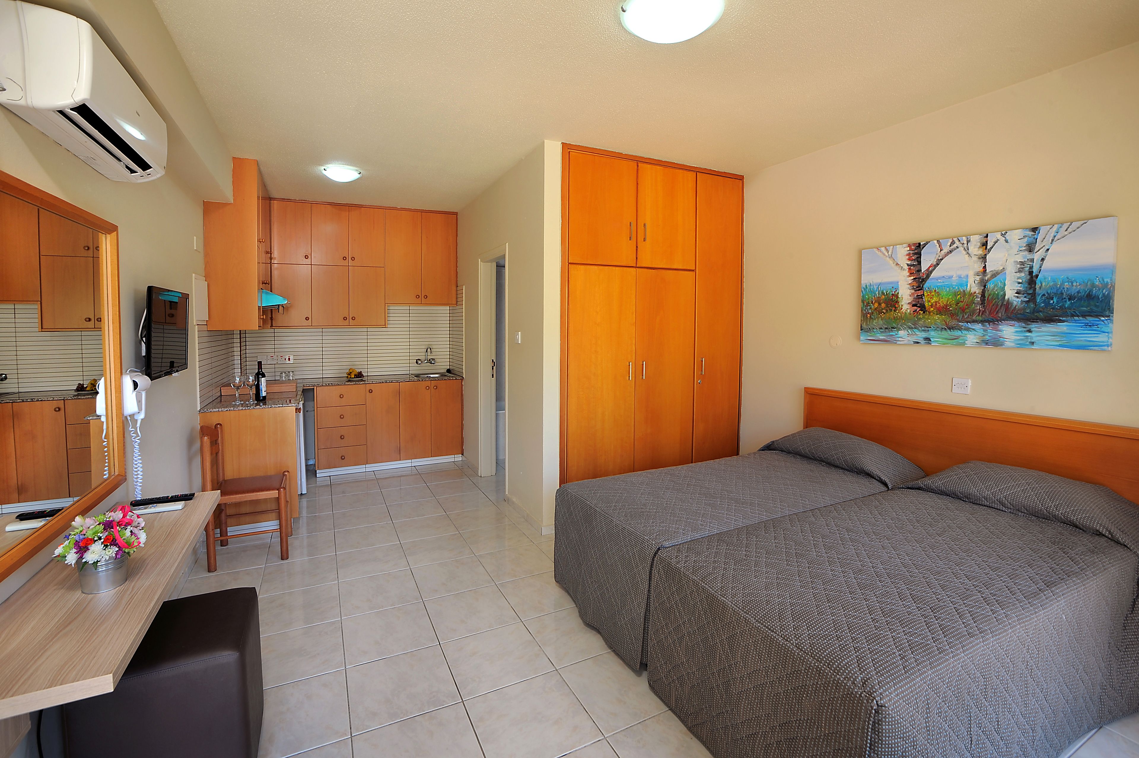Une petite pièce comprenant un lit, un bureau avec une chaise, un coin cuisine et un tableau accroché au mur.
