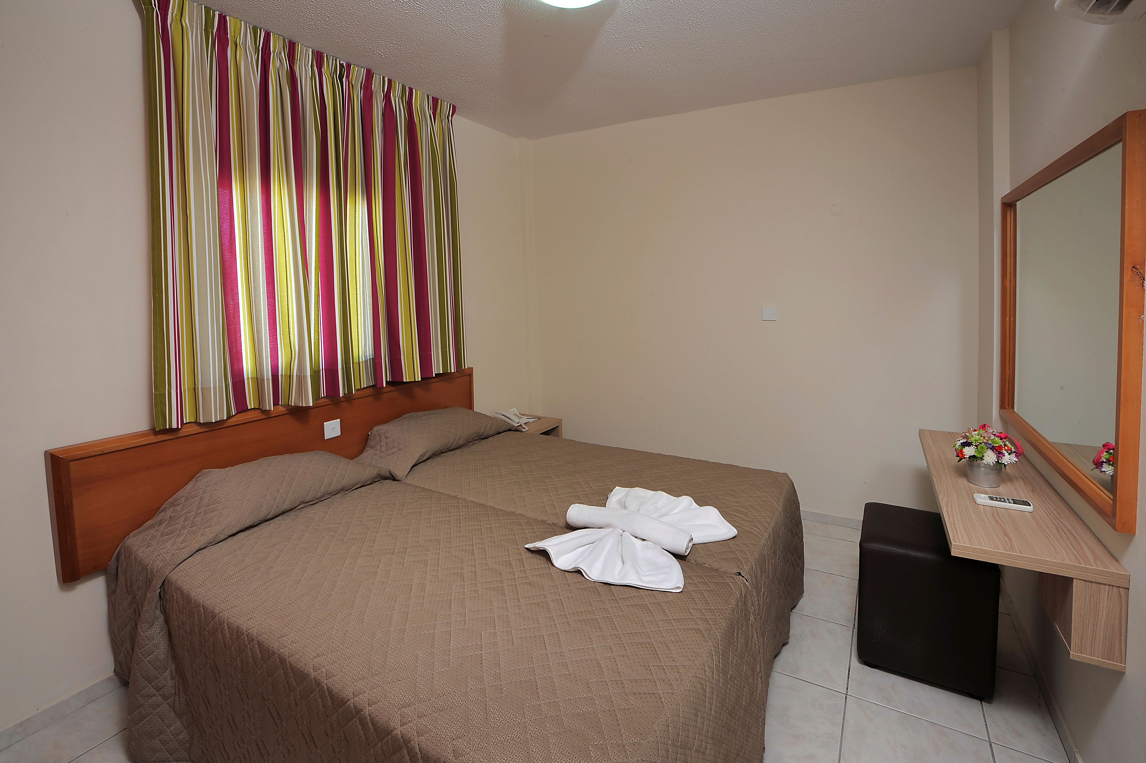Una habitación de hotel con una cama, un escritorio con espejo y una ventana con cortinas.