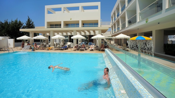 Una piscina con gente, sillas de descanso y sombrillas.
