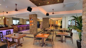 Un amplio comedor interior con varias mesas y sillas de madera, una zona de bar con taburetes y una planta grande en maceta.
