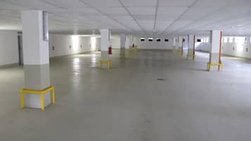A spacious indoor area with white walls and a tiled ceiling, featuring several pillars with yellow bases and a fire extinguisher mounted on one pillar.
