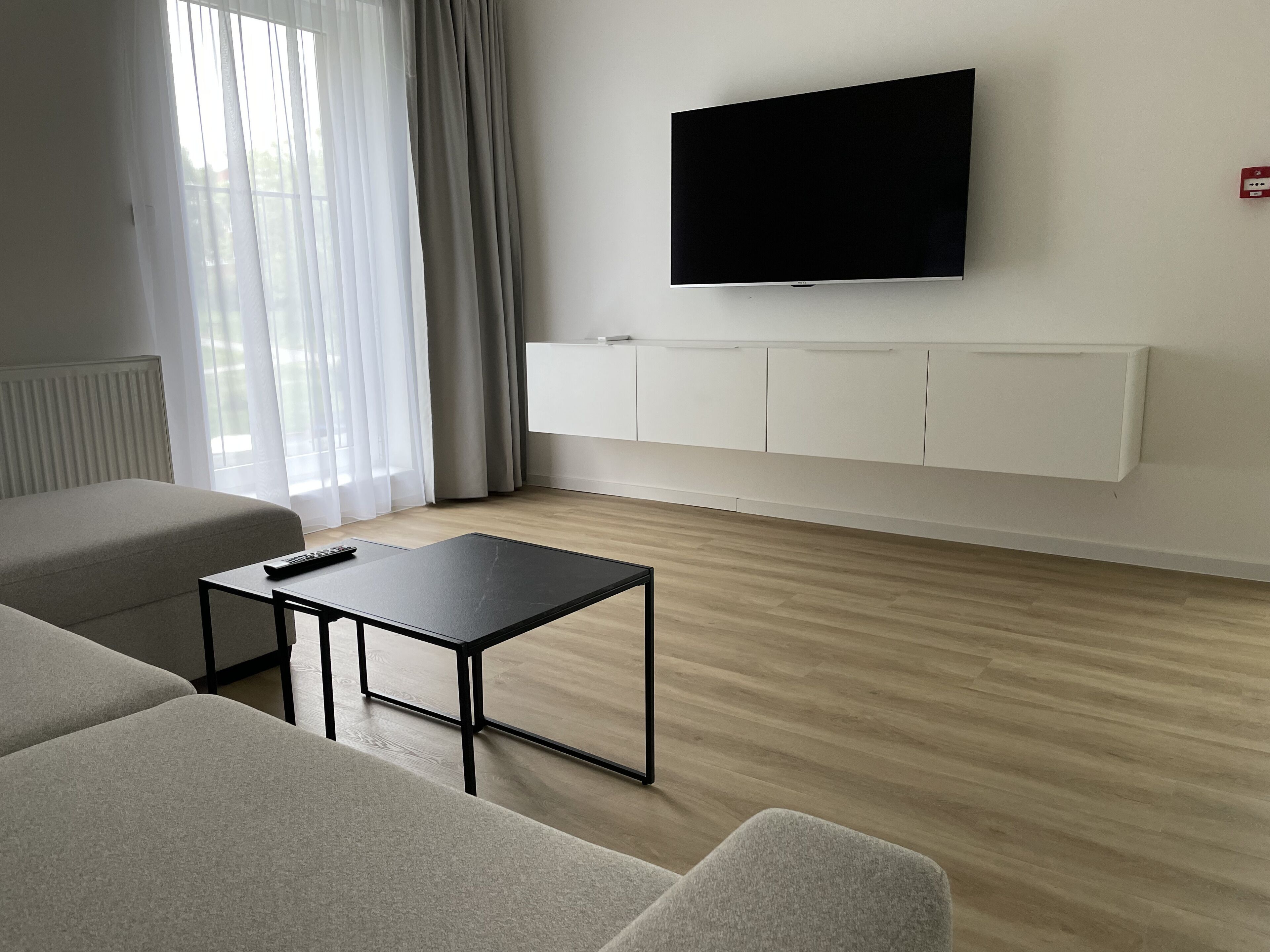 Een moderne woonkamer met een flatscreen televisie aan de muur, een kleine zwarte tafel en twee grijze banken.